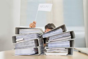 business man behind a pile of paperwork holding help sign | Timeline Software for Law Firms