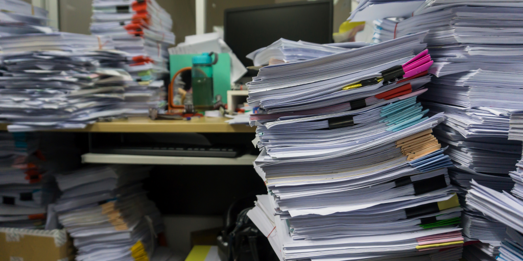 A pile of papers in a cluttered office desk, explaining the importance of a legal timeline software.